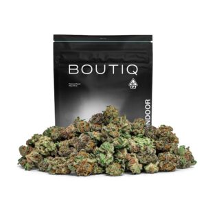 A pile of vibrant green cannabis buds in front of a black BOUTIQ brand pouch, which labels the product as 'Premium Flower 14g | 0.5oz' and 'INDOOR' with a CA cannabis symbol.